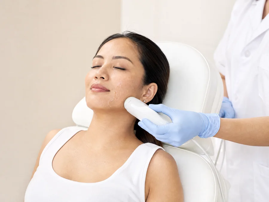 A practitioner moving an ultrasound handpiece along a woman's jawline